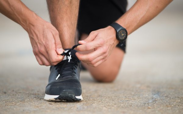 Homem amarrando um cadarço de um tênis de corrida
