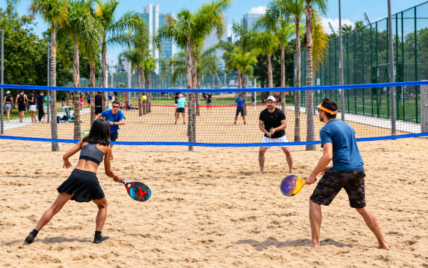 Pessoas jogando beach tennis em quadra de areia ao ar livre